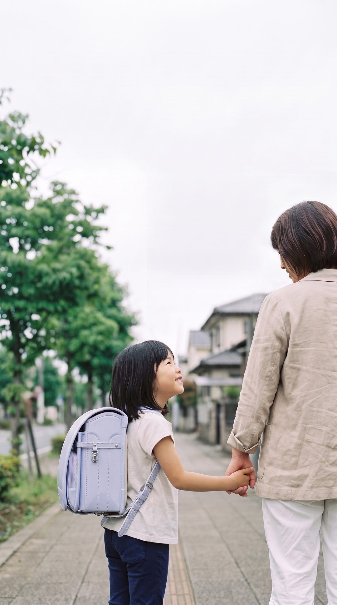 母親と手をつなぎ、笑顔で見上げながら歩く小学生